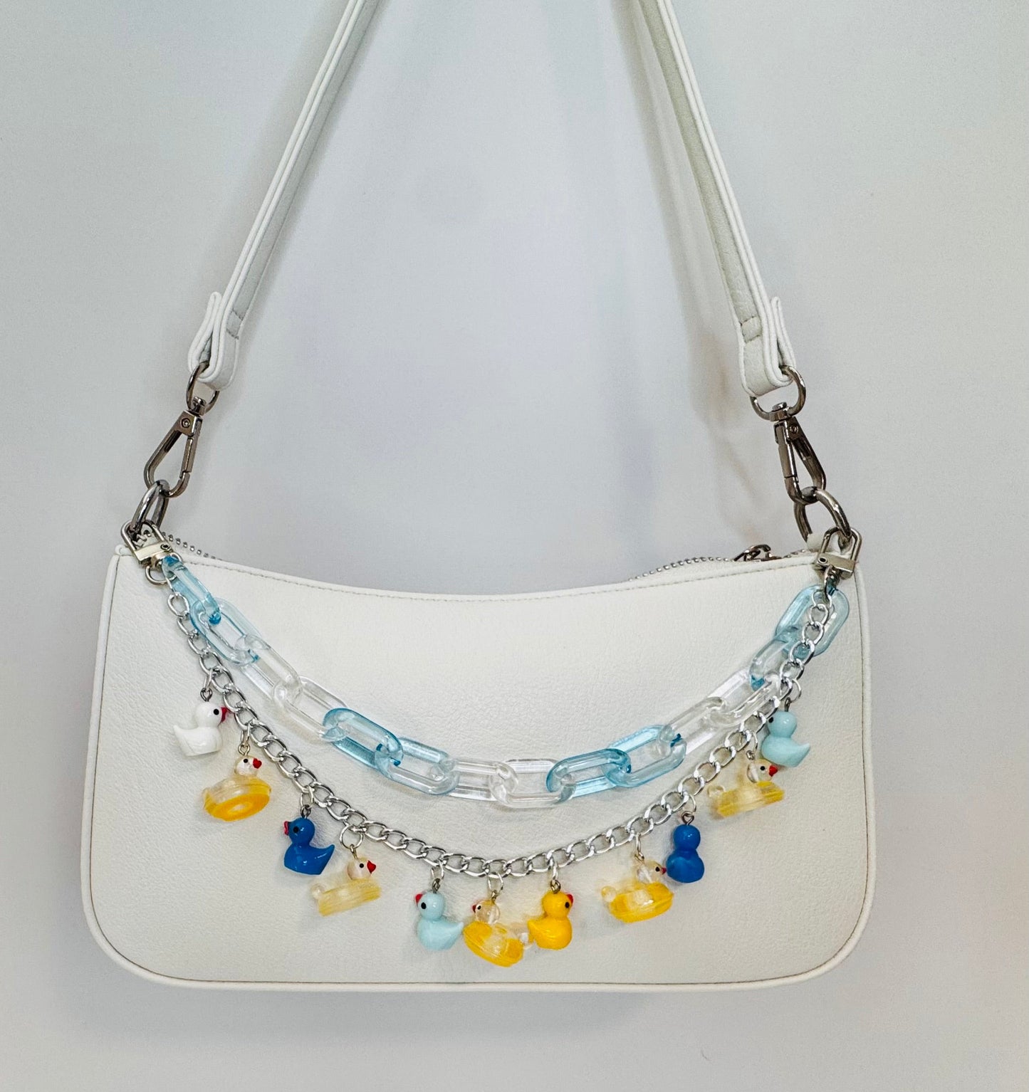 White handbag with colorful charm chain on a light gray background