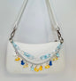 White handbag with colorful charm chain on a light gray background
